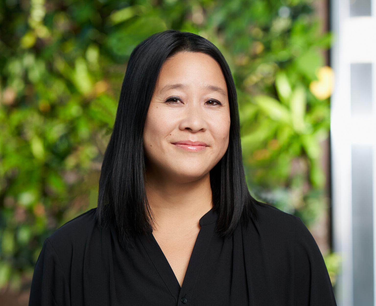 Smiling person wearing black in front of a lush green background