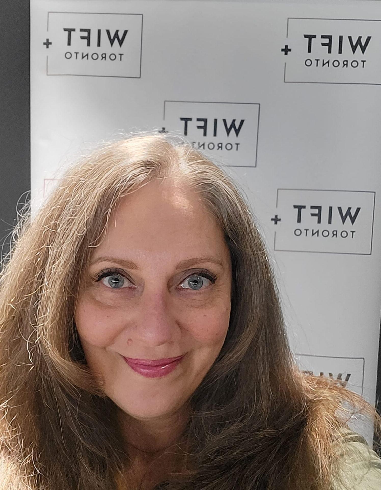 Close up selfie of a person smiling in front of a WIFT+ Banner